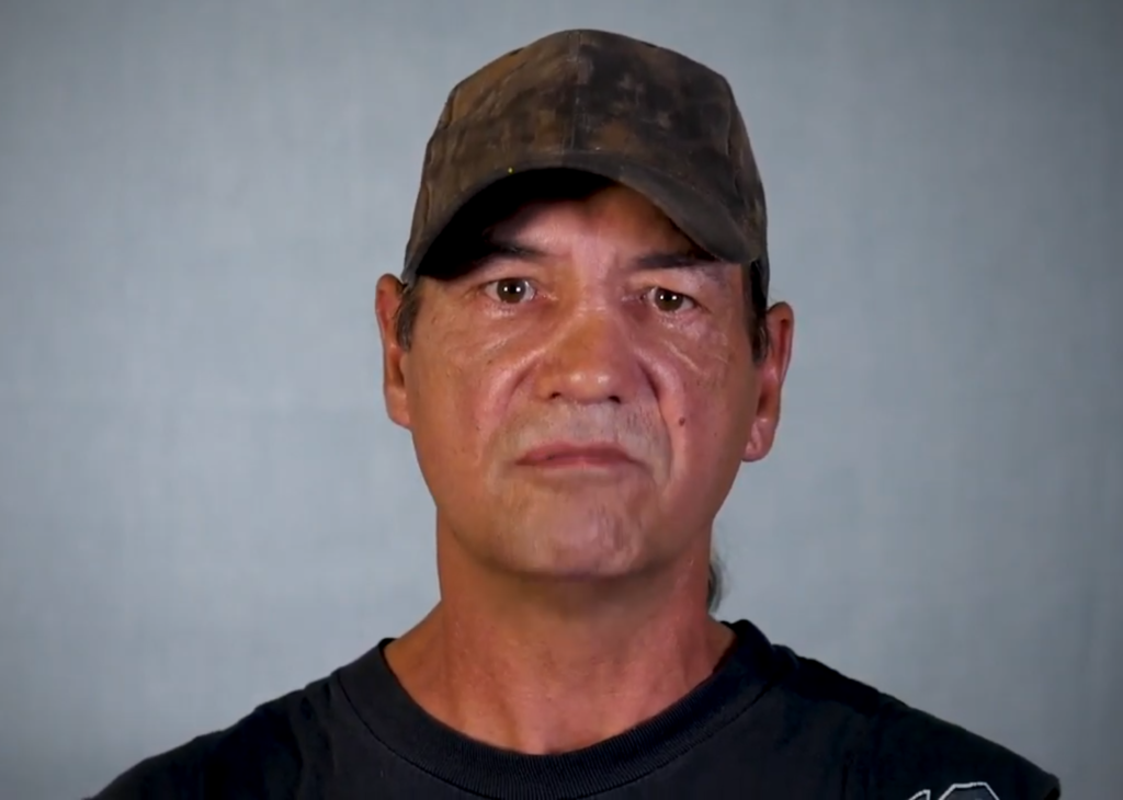 An indigenous man in a brown hat and black shirt.